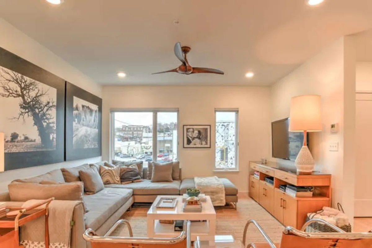 This shot features a generous sectional sofa, stylish wall art, and a modern light fixture, with a TV console that adds to the ambiance. The room radiates contemporary comfort and is clearly designed for socializing, movie nights, or relaxed mornings, echoing the urban social living theme.