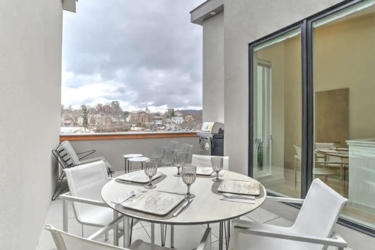 The photo features a rooftop dining table set up for al fresco meals, with a grill nearby and open views stretching across the landscape. The patio's layout is primed for both group gatherings and quiet moments, with the warm glow of sunset hinting at magical evenings spent here.