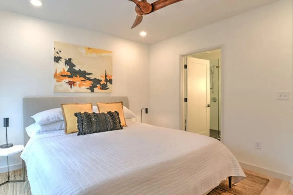 A tranquil bedroom with a comfortable bed adorned with decorative pillows, artwork above the headboard, and a nightstand with a soft-glow lamp. The room is softly lit and feels private and cozy, perfect for unwinding or catching up on sleep.