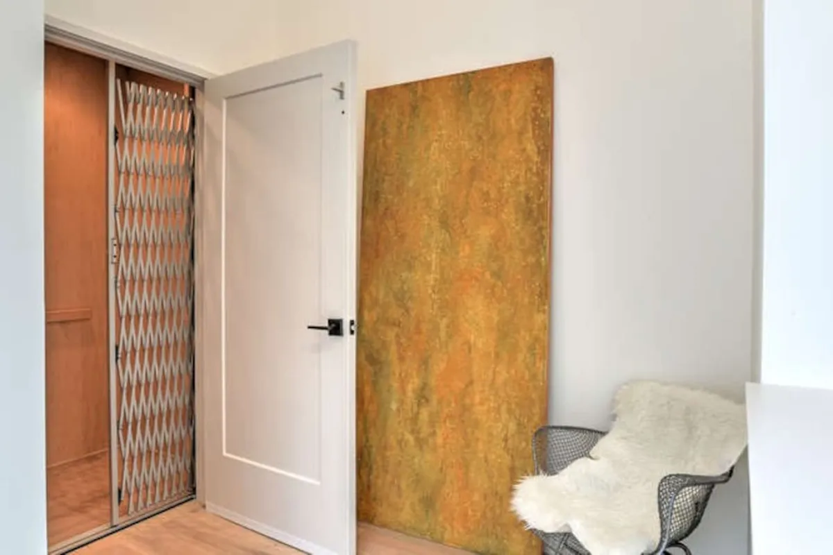 A stylish, contemporary entry area with an elevator door, modern art on the wall, and a chair with a fur throw. The space hints at access to other building features, including rooftop or communal spaces.