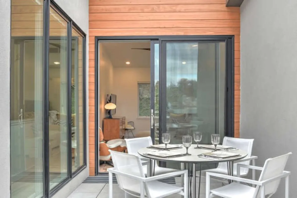 This image presents an outdoor dining table on a rooftop, framed by sliding glass doors that seamlessly connect the interior to the exterior space. The setup suggests effortless transitions between indoor comfort and open-air enjoyment, with views that extend beyond the immediate patio.
