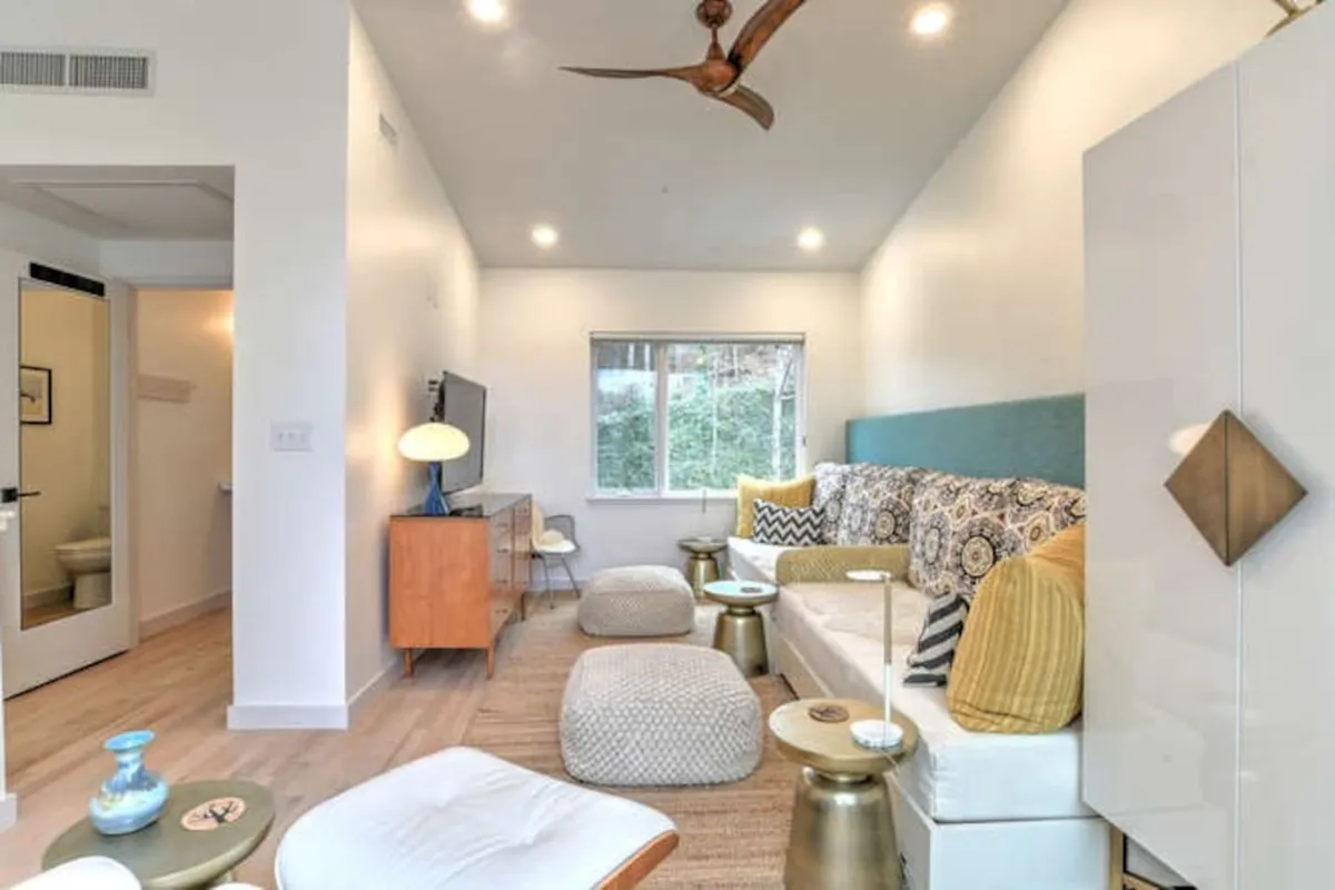 A comfortable, stylish living area featuring a sofa with patterned cushions, a wooden coffee table, a decorative lamp, and a large window letting in abundant natural light—suggesting a connection between indoor relaxation and views of the outdoors.