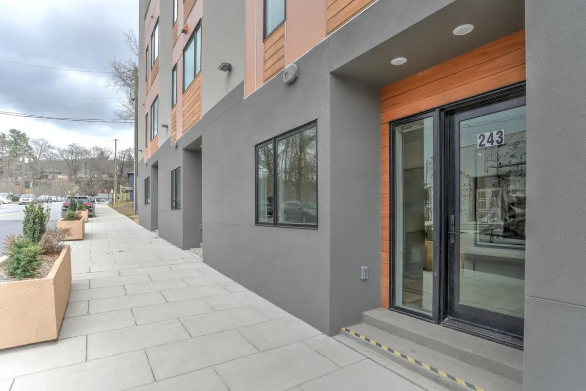This image features the modern entrance of the property, with large windows, a clean sidewalk, and lush planters. The inviting facade suggests easy access to the residence and hints at a welcoming, community-focused environment right in the heart of downtown.
