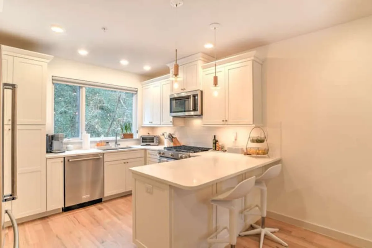 A contemporary kitchen with a spacious island stands out, accented by pendant lighting and stainless steel appliances. Large windows flood the space with sunlight, echoing the narrative’s focus on natural light and the central hub for meal preparation, conversation, and socializing.