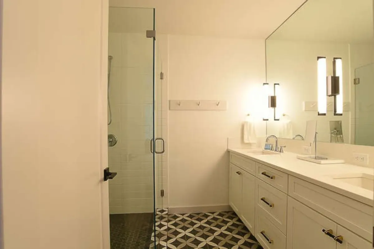 A fresh and modern bathroom with a glass shower enclosure, patterned floor tiles, and a double vanity topped with a large mirror. The space is bright and feels inviting, designed for both style and comfort.